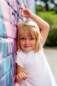 Prämie; Mädchen lehnt an einer bunten Wand und lächelt.