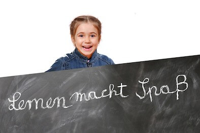 Kind an einer Tafel mit der Aufschrift Lernen macht Spaß!