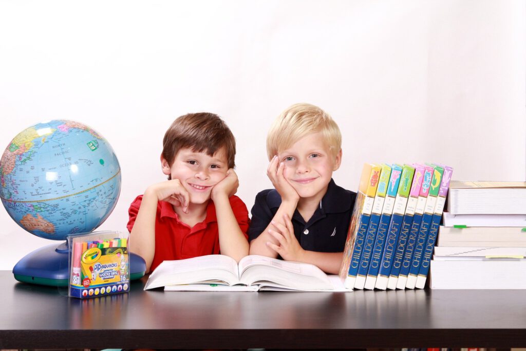 2 Jungs schauen lächelnd in die Kamera. Auf dem Tisch sind Bücher und ein Globus